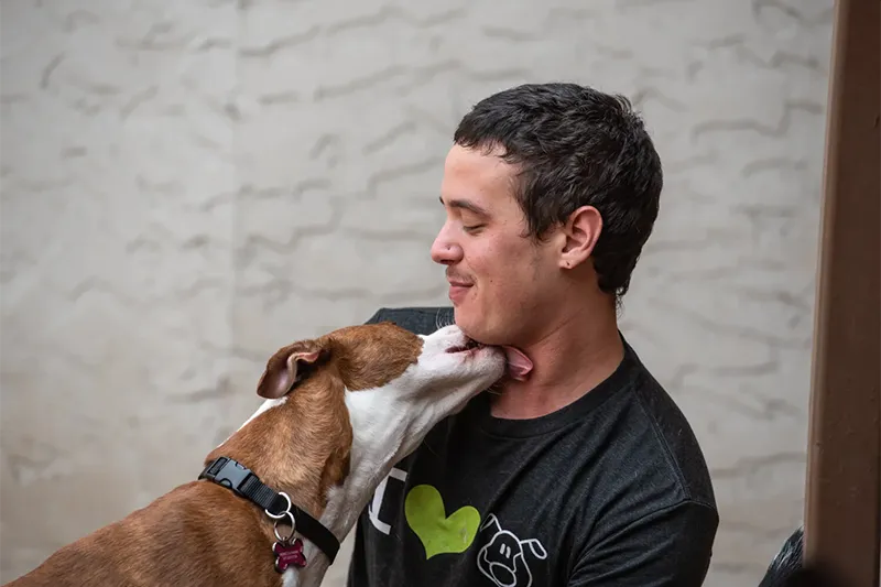 A dog licks an employees neck affectionately as he smiles
